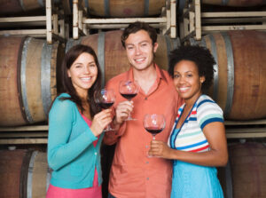3 young friends wine tasting among wine barrels